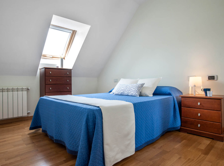 Dormitorio matrimonio con textiles azules y blancos en planta alta dúplex urbanización Riobao, Sada_velux
