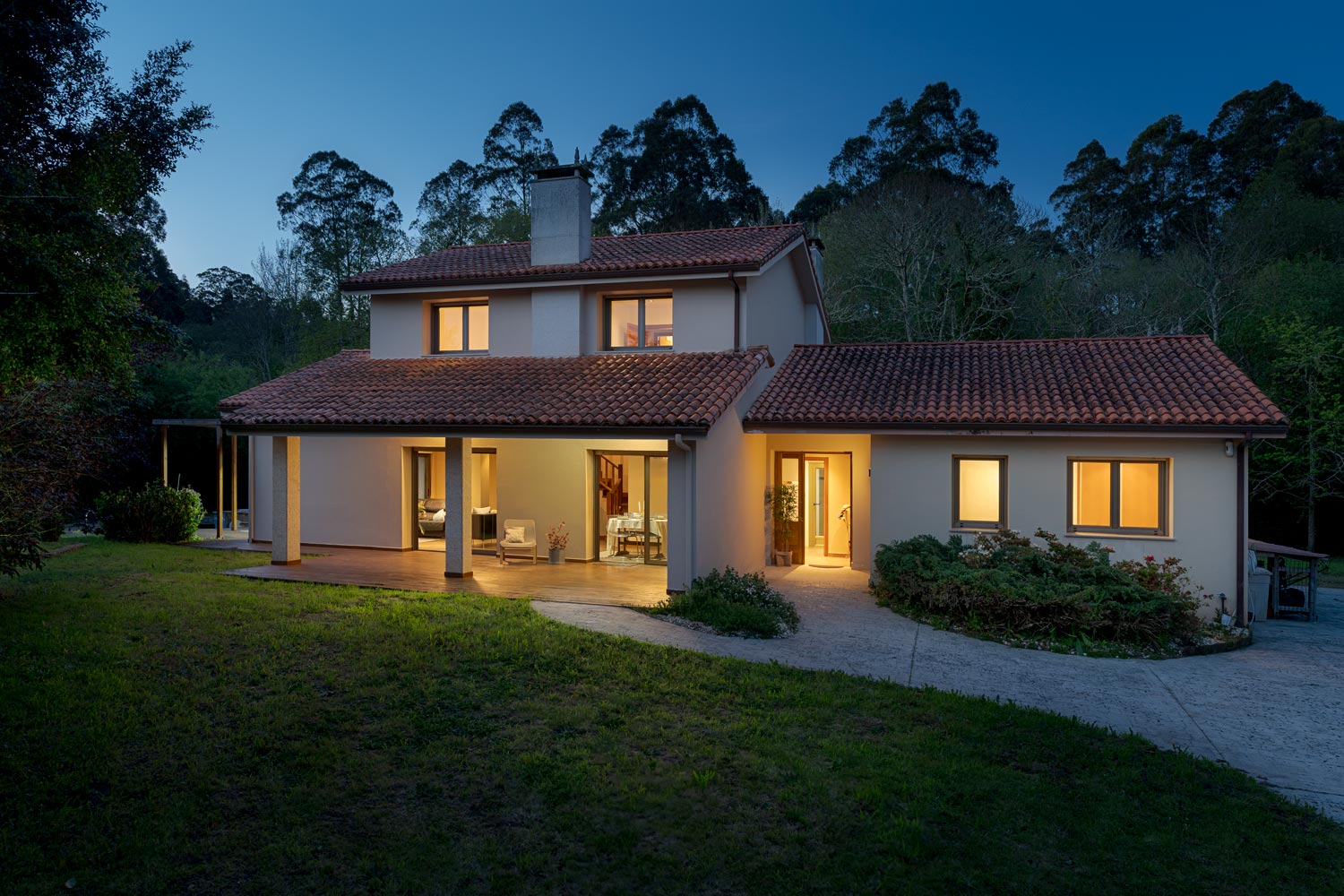 Acogedora casa unifamiliar iluminada al atardecer con techo de tejas, rodeada de un jardín verde y árboles, mostrando una sensación de hogar y tranquilidad en un entorno natural.