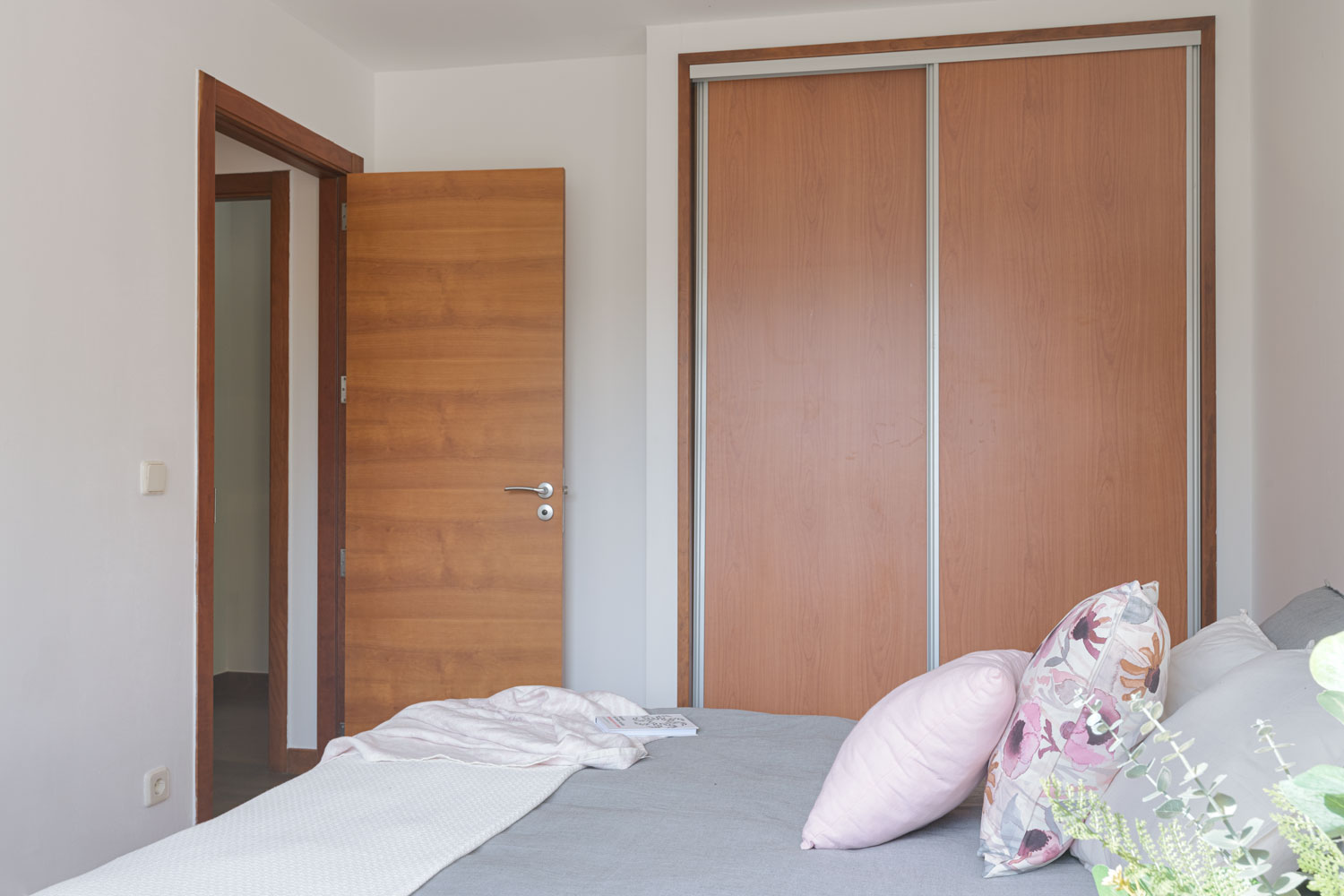 Interior minimalista con puerta de madera, armario empotrado grande y una cama con ropa de cama suave, destacando un diseño funcional y tranquilo