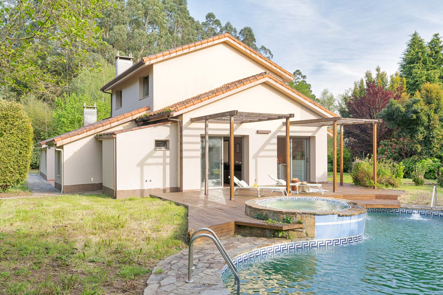 Casa moderna con piscina y jacuzzi en un exuberante jardín verde, con una amplia terraza de madera y zona de relax al aire libre