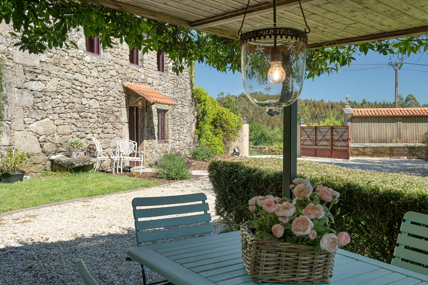 Casa rústica en venta en Aranga por Inmobiliaria Morando, con fachada de piedra, tejado de tejas rojas, área de comedor exterior y jardín con flores.