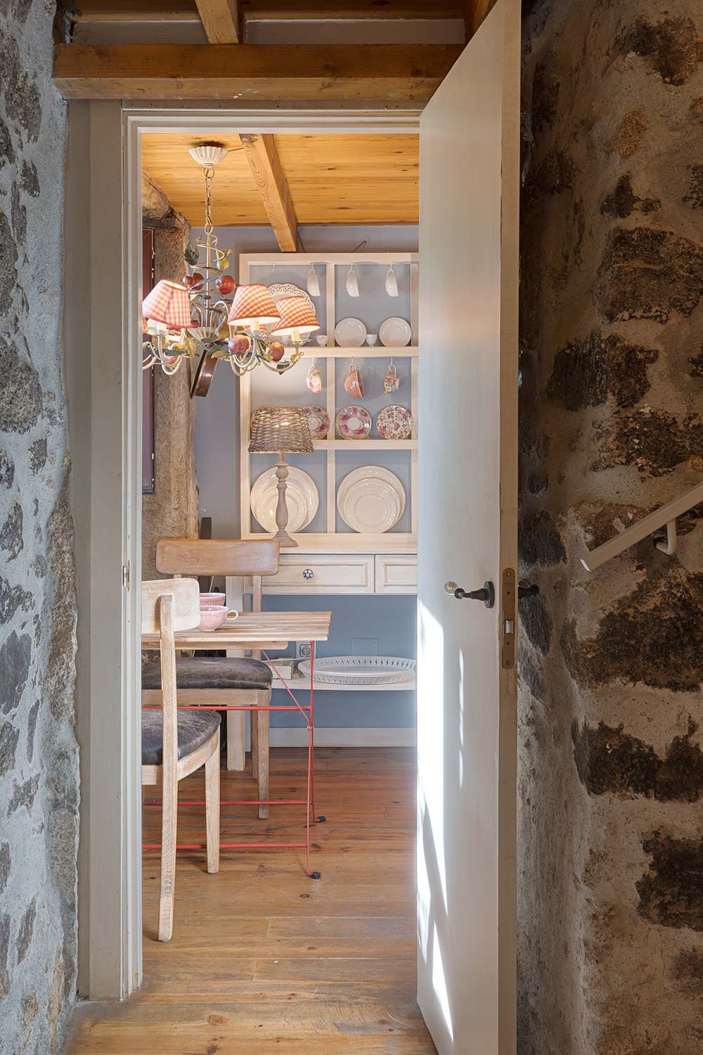 Vista de una acogedora cocina rústica desde la puerta, con una mesa pequeña y estantes con platos decorativos.