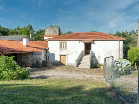 "Casa en venta en Bergondo con tejado de tejas rojas, pozo de agua, jardín y camino de acceso, bajo un cielo azul."