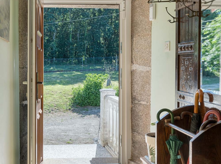 "Entrada de casa en venta en Bergondo, con vista al exterior, suelo de baldosas, paragüero de madera y luz natural."