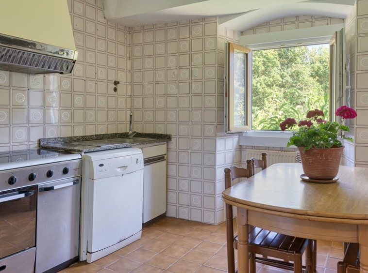 "Cocina en casa en venta en Bergondo, con azulejos decorativos, estufa y lavavajillas, mesa de comedor de madera y una ventana abierta con vistas al jardín."