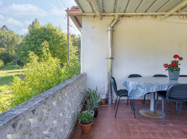 "Terraza en una casa en Bergondo con mesa redonda, sillas negras y plantas en macetas, con vistas al jardín y árboles"