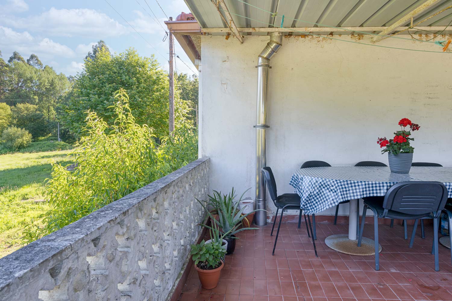 "Terraza en una casa en Bergondo con mesa redonda, sillas negras y plantas en macetas, con vistas al jardín y árboles"