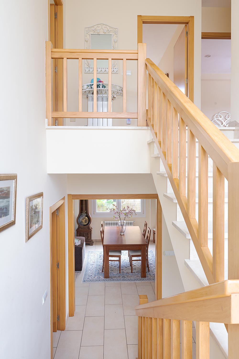 Vista desde una escalera de madera hacia un comedor con mesa de madera y sillas, alfombra clara y detalles decorativos. En venta por Morando Inmobiliaria