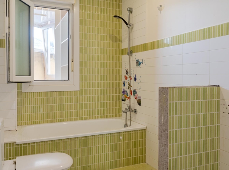 Baño con azulejos verdes y blancos, bañera y ventana abierta. Decoración infantil con peces en la pared. En venta por Morando Inmobiliaria