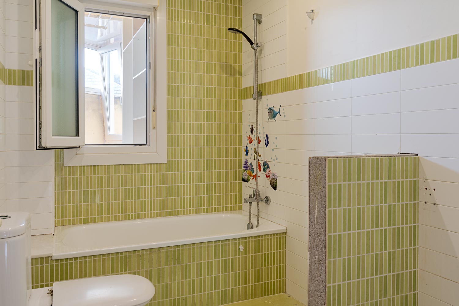 Baño con azulejos verdes y blancos, bañera y ventana abierta. Decoración infantil con peces en la pared. En venta por Morando Inmobiliaria