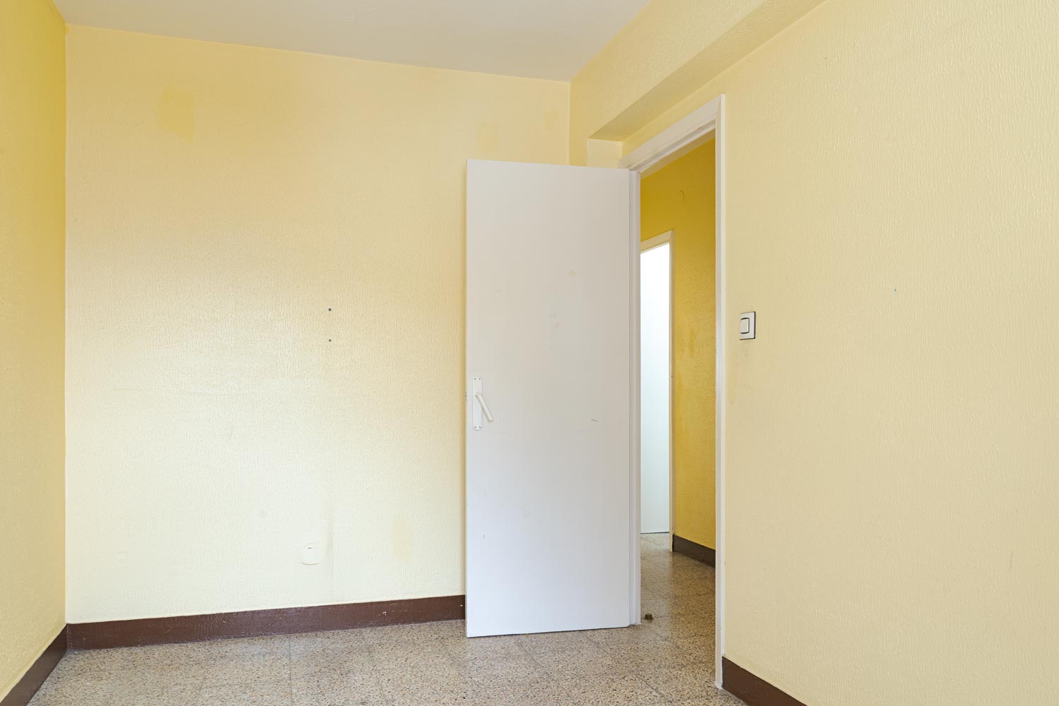 Entrada de habitación con puerta blanca y paredes amarillas en apartamento de Sada.