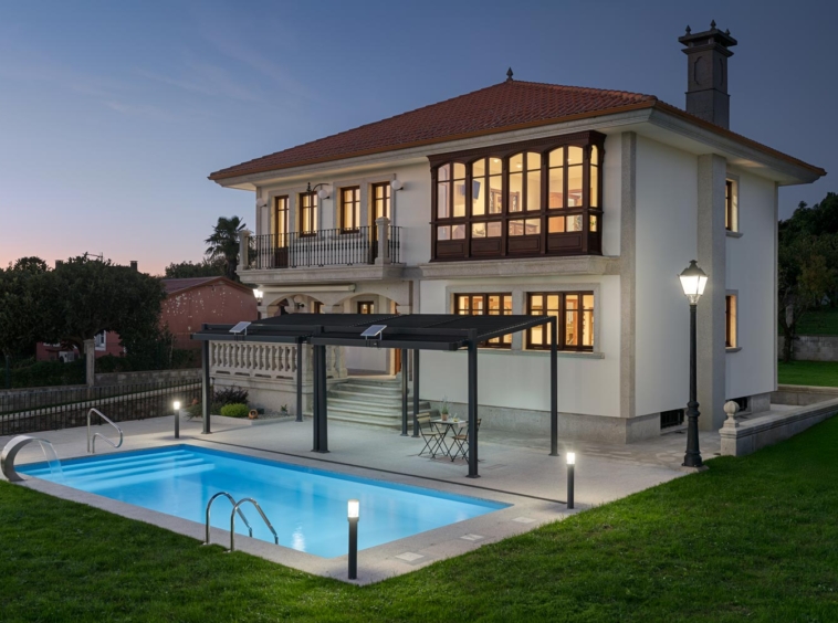 Casa en Bergondo con iluminación nocturna, fachada elegante y piscina iluminada. Venta exclusiva de Inmobiliaria Morando.